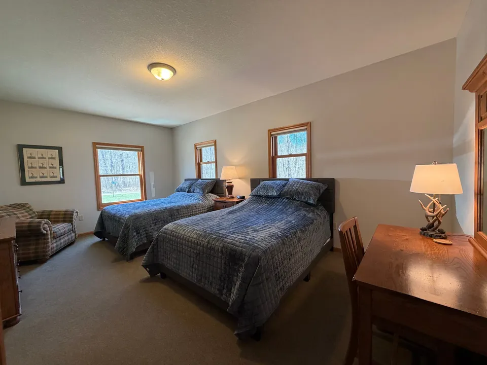 Cottage bedroom with two queen beds, blue quilted bedding, and bright windows looking onto the trees