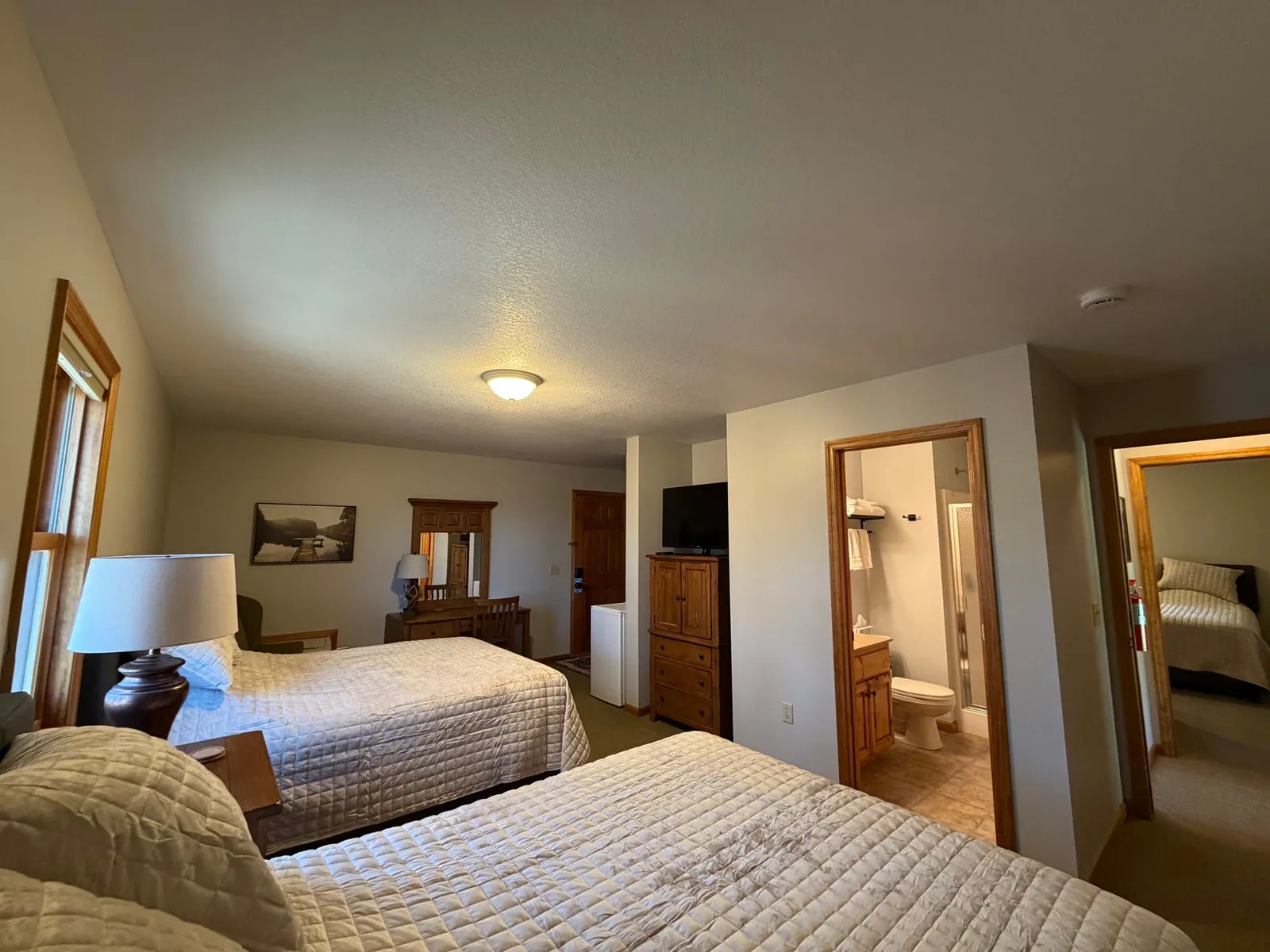 Cottage bedroom with two queen beds, cream quilted bedding, and a private en-suite bathroom