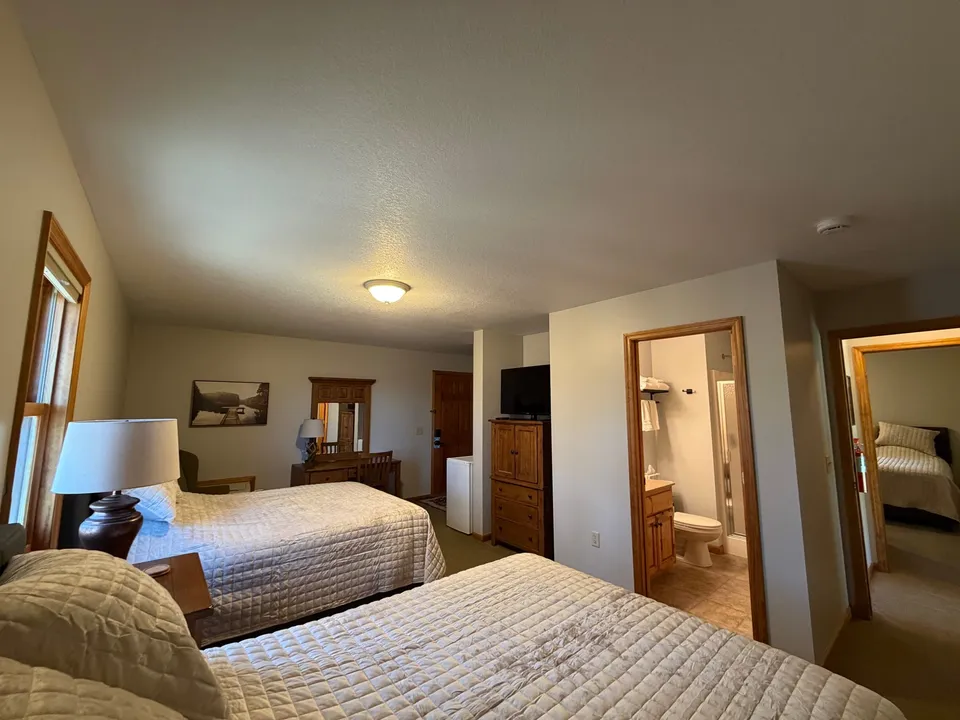 Cottage bedroom with two queen beds, cream quilted bedding, and a private en-suite bathroom