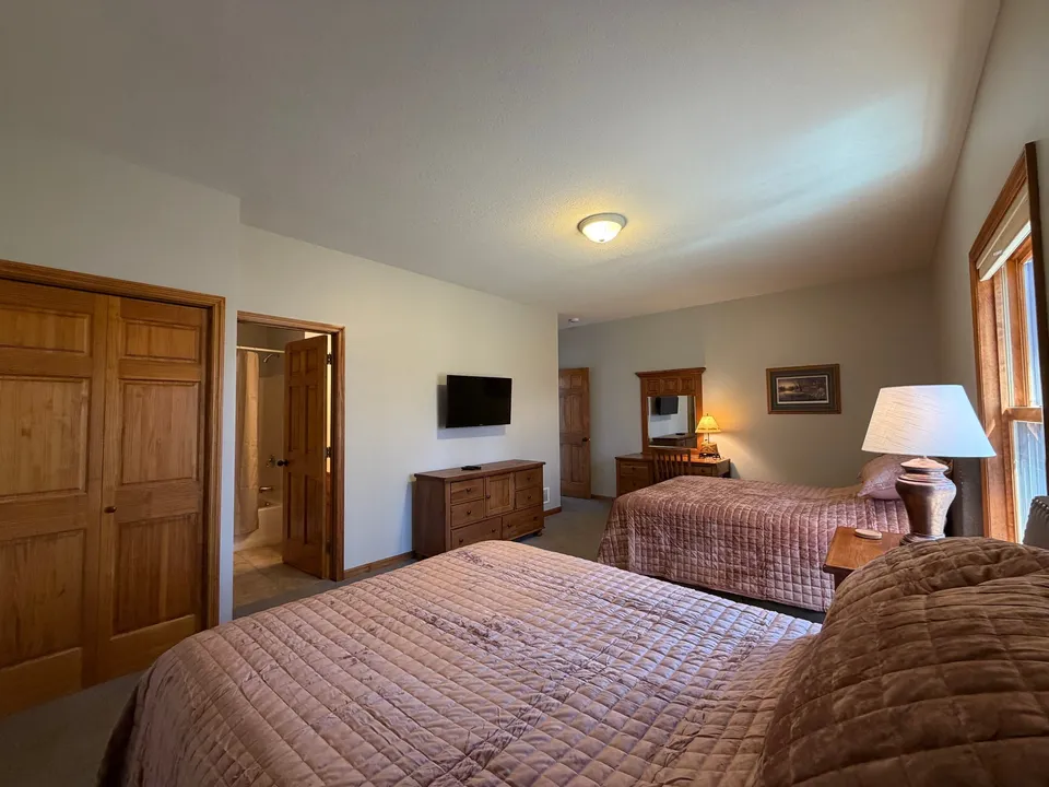 Tan-quilt bedroom inside the cottage with bright natural light from a tall window and en-suite entry