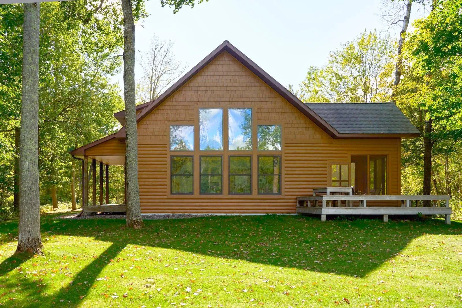 The Cottage at Golden Eagle, a cedar-sided cabin with a peaked wall of windows, set among Northwoods hardwoods
