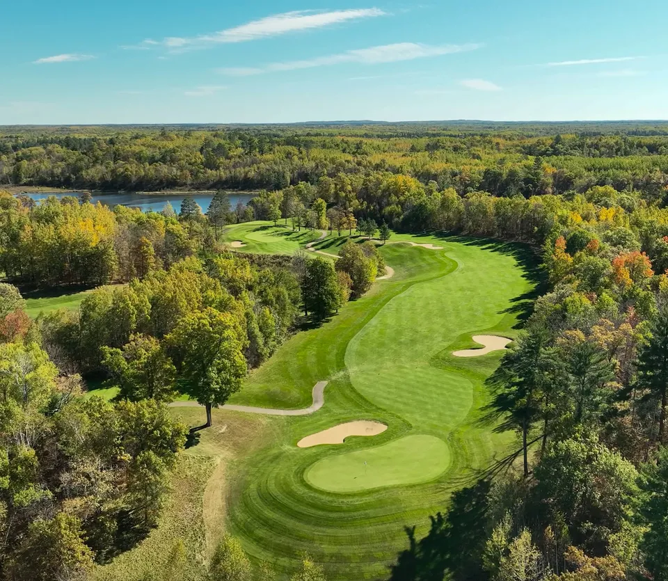 Mid-summer fairway in full green from an elevated tee, distant treeline along the horizon