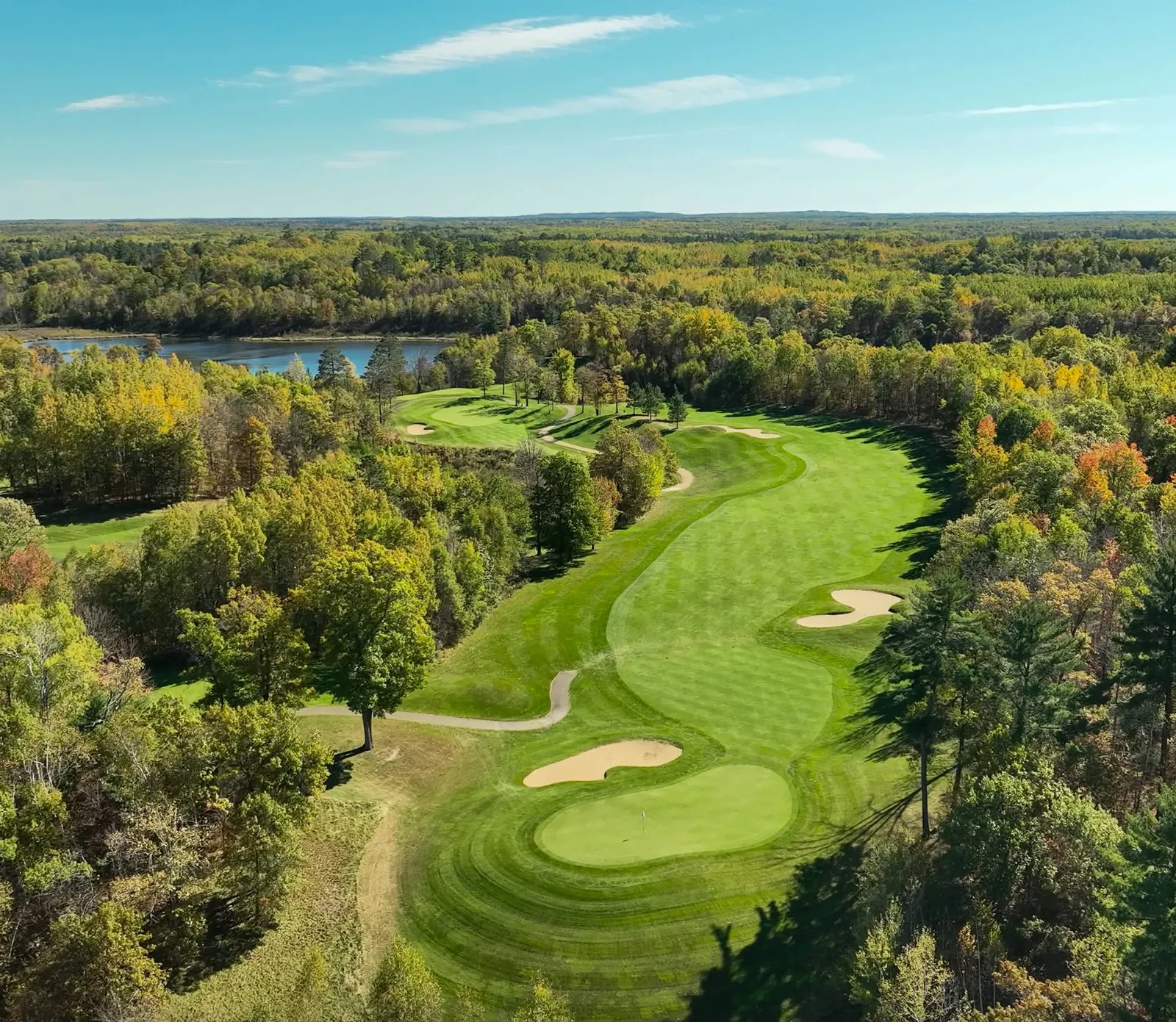 Mid-summer fairway in full green from an elevated tee, distant treeline along the horizon