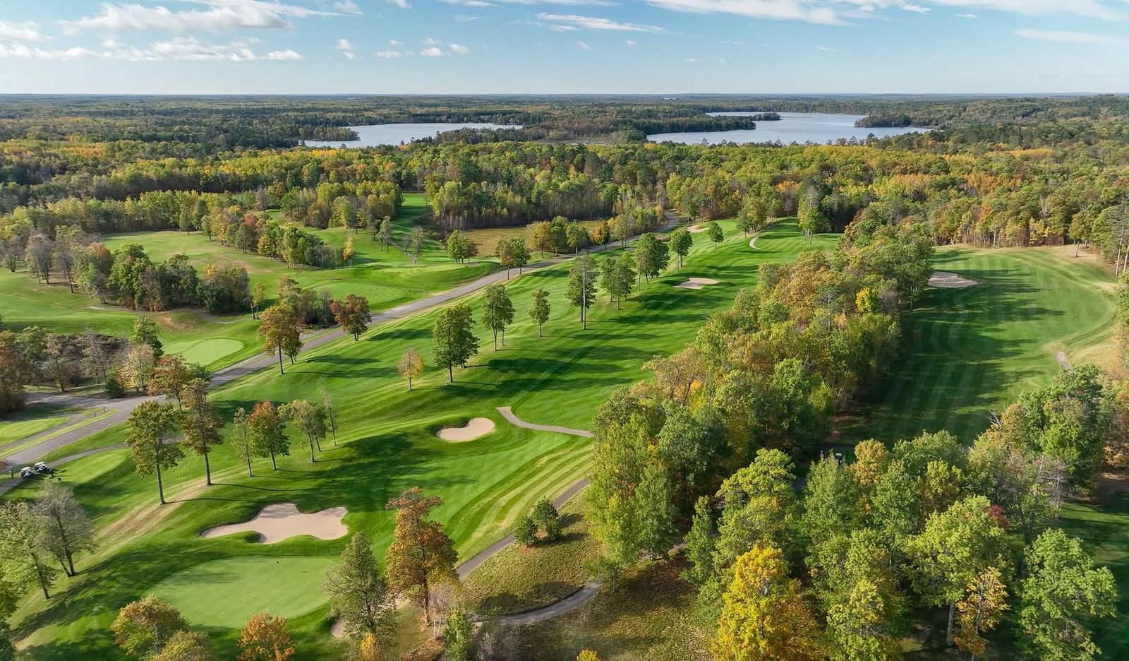 Fall fairway lined with red-and-gold maples winding back toward the clubhouse
