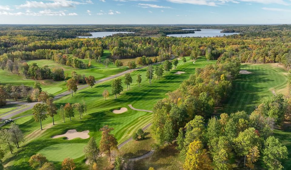 Fall fairway lined with red-and-gold maples winding back toward the clubhouse