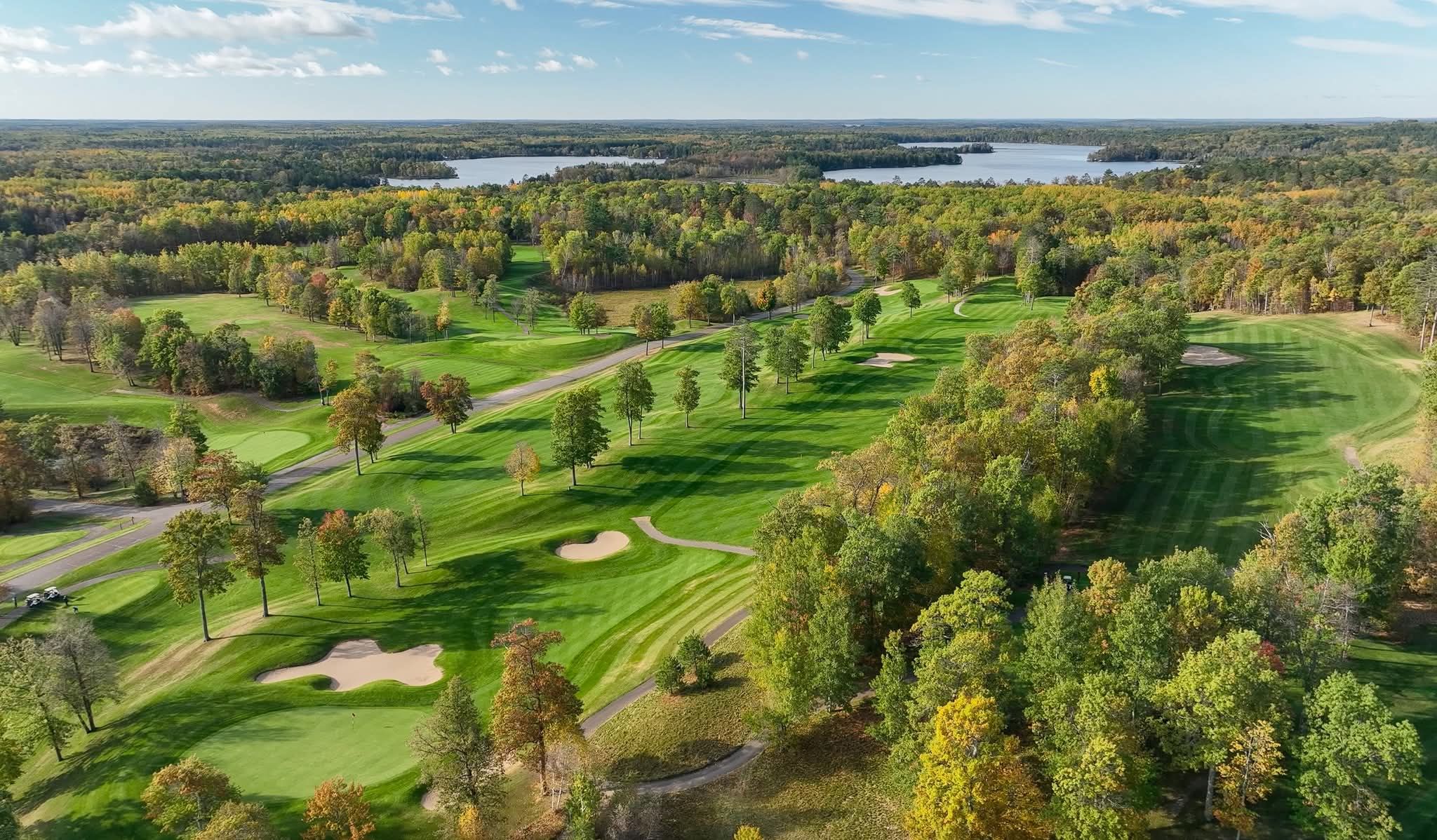 Fall fairway lined with red-and-gold maples winding back toward the clubhouse