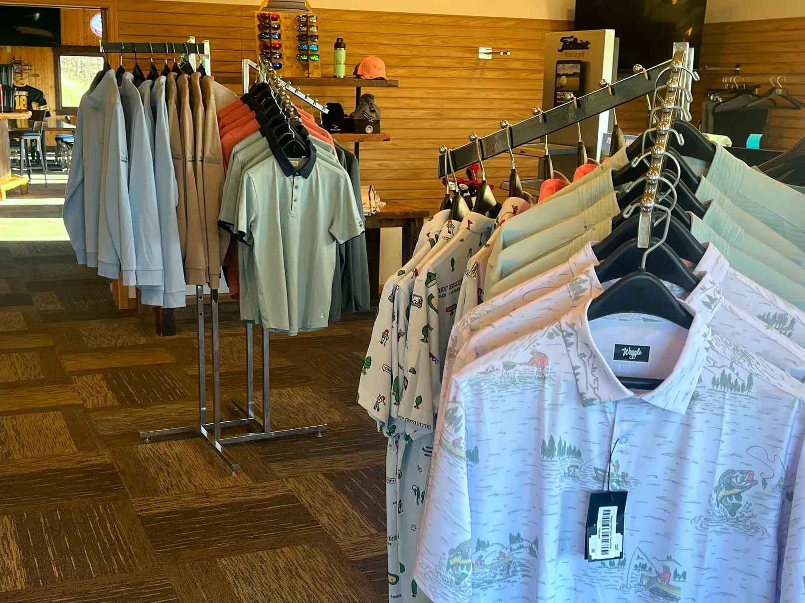 Racks of Waggle patterned polos and quarter-zip pullovers inside the Golden Eagle pro shop, with sunglasses, hats, and Titleist display in the background