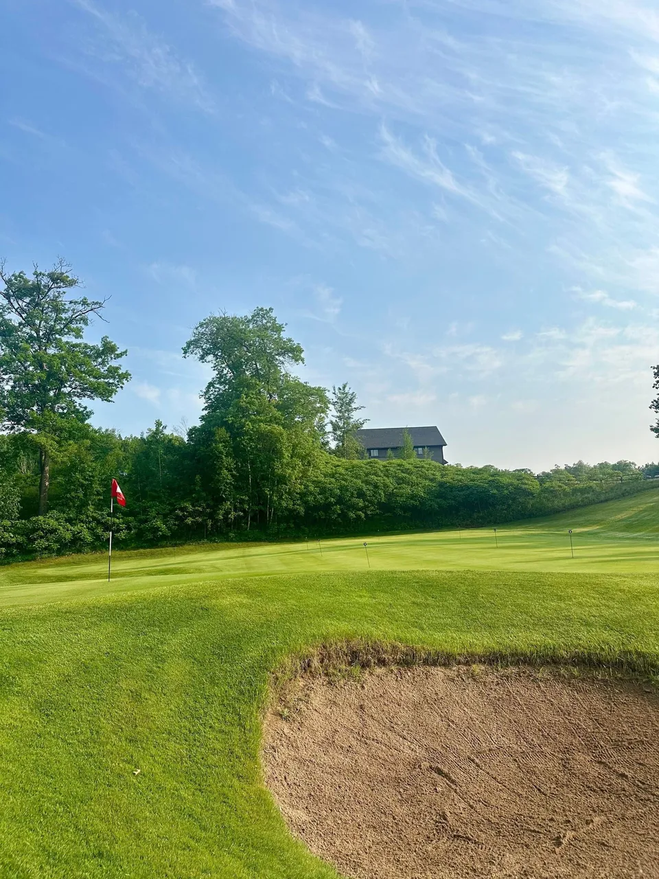 Greenside bunker raked smooth in late-day sun, fairway curving beyond