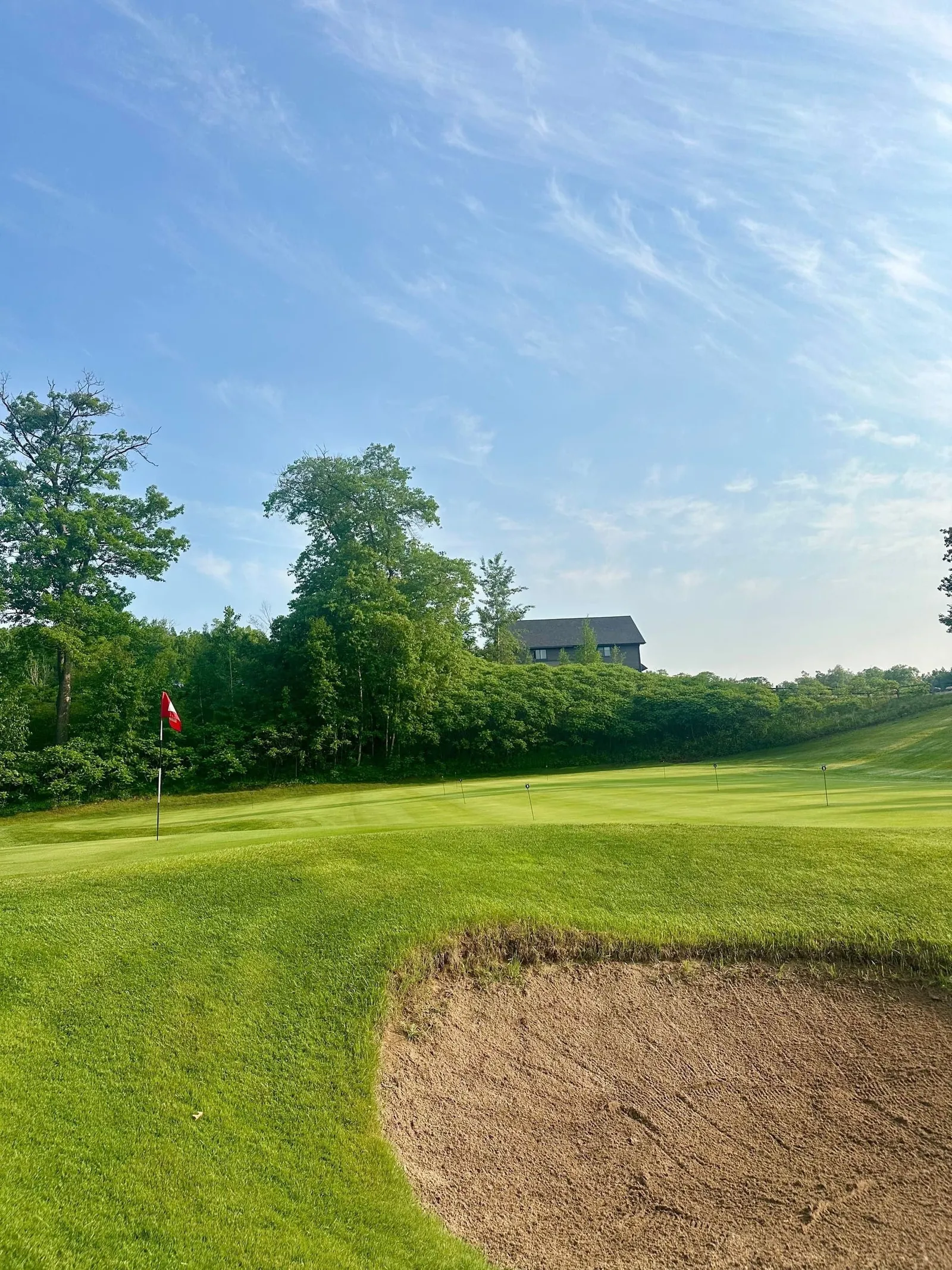 Greenside bunker raked smooth in late-day sun, fairway curving beyond