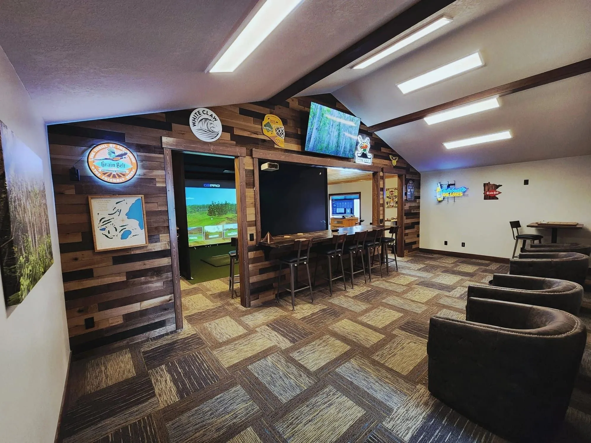Wide view of the upstairs Golden Eagle simulator lounge with comfortable seating and the GSPro screen