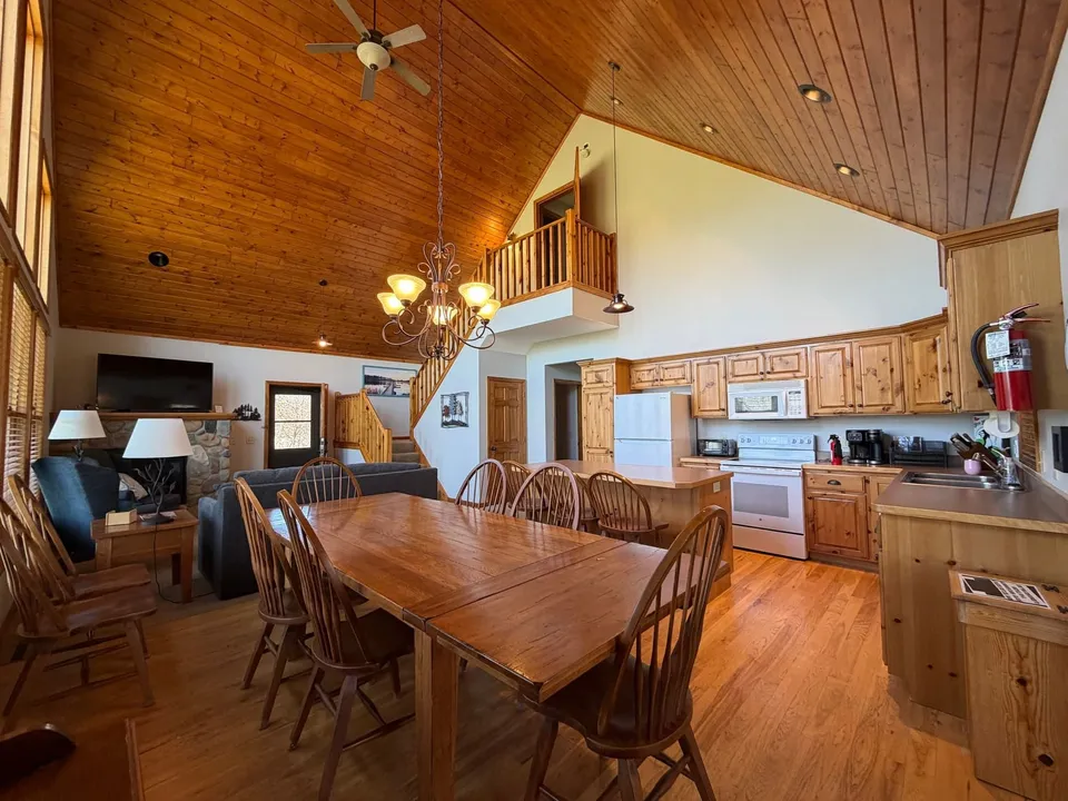 Open great room inside the Golden Eagle Cottage: long dining table, full kitchen, and vaulted pine ceiling with loft above