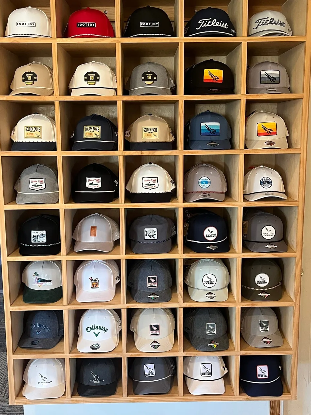 Wall of hat cubbies in the Golden Eagle pro shop stocked with TravisMathew, Branded Bills, FootJoy, Waggle, and Pukka headwear