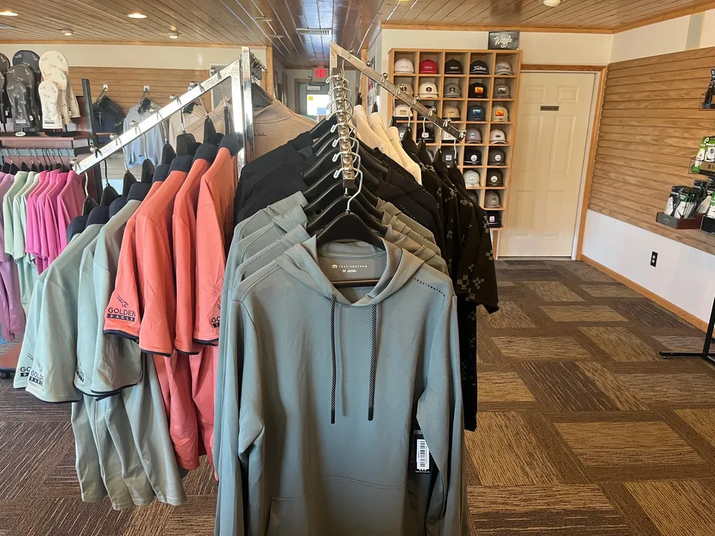Hoodies and quarter-zips on a rack in the Golden Eagle pro shop with the hat wall in the background