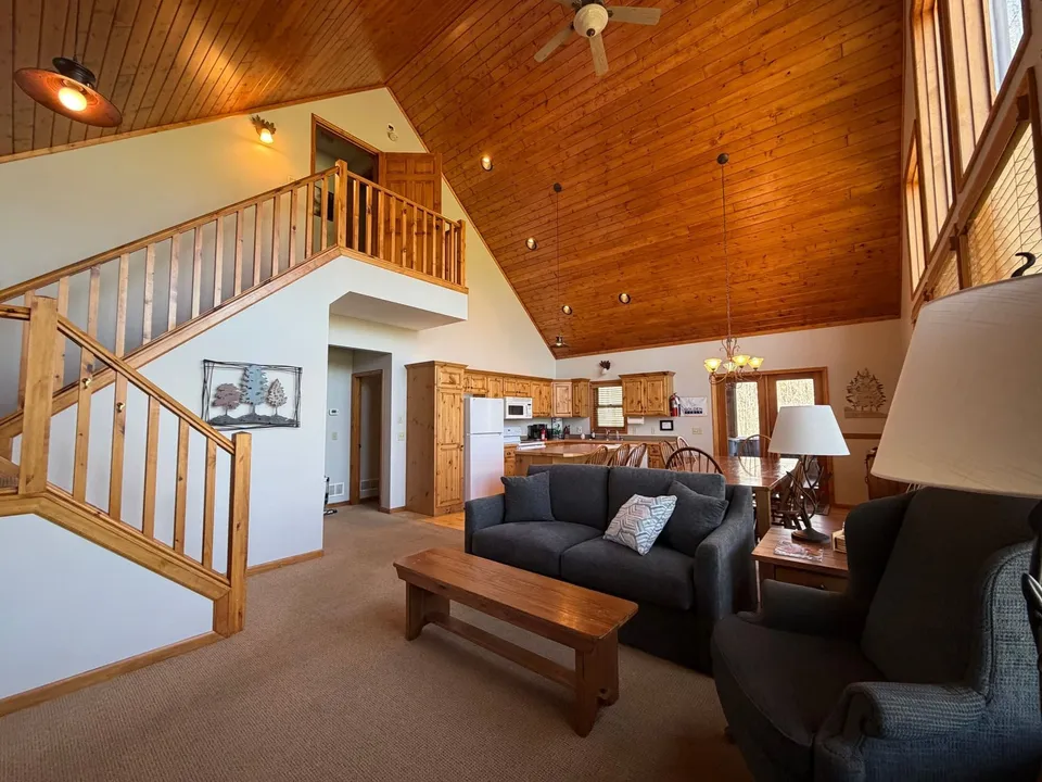 Living room inside the Golden Eagle Cottage with an open staircase leading up to the loft and vaulted pine ceiling overhead