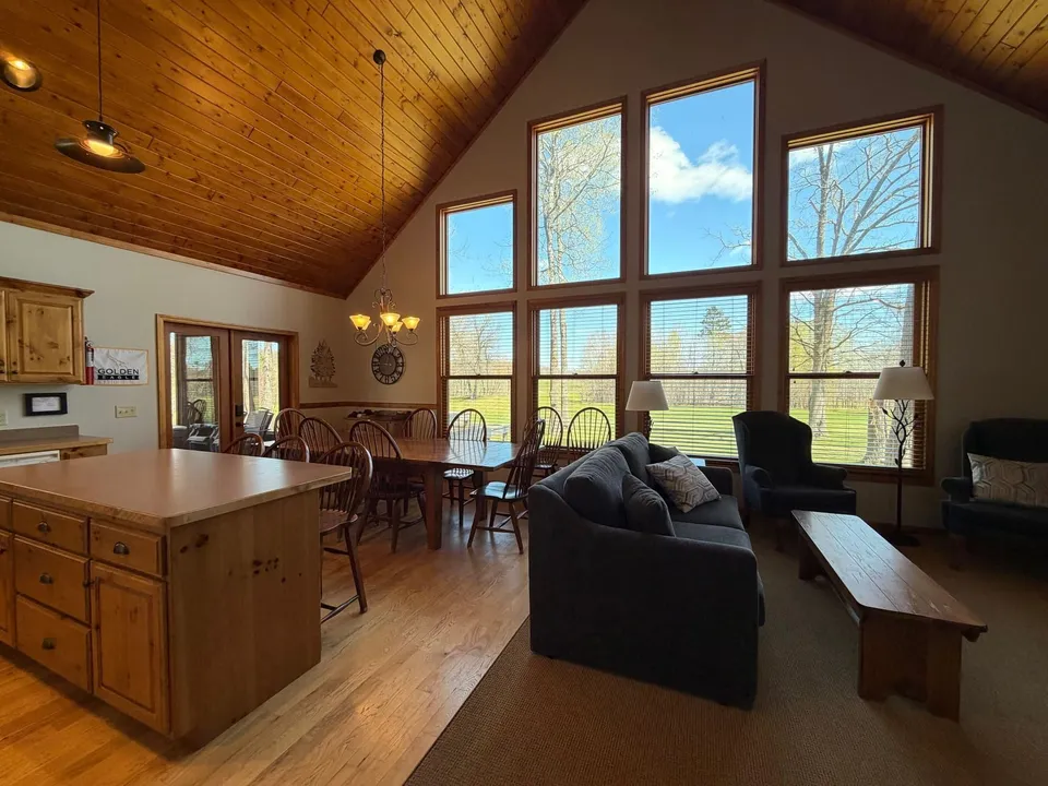 Living and dining area at the cottage backed by a full wall of windows looking onto the course
