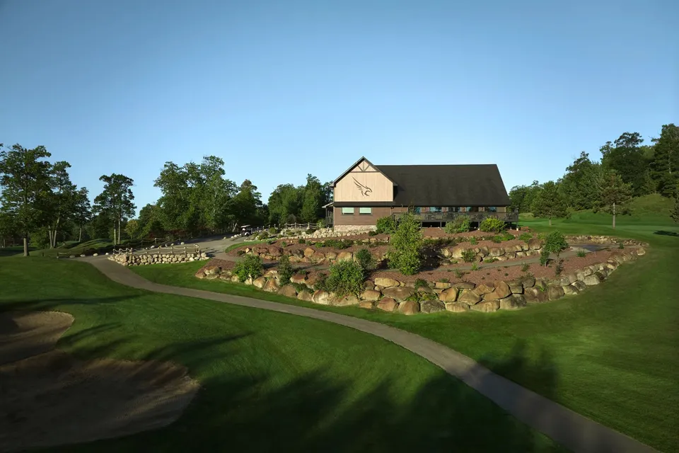 The Golden Eagle clubhouse rising above a rock-walled berm with a fairway, bunker, and cart path in the foreground