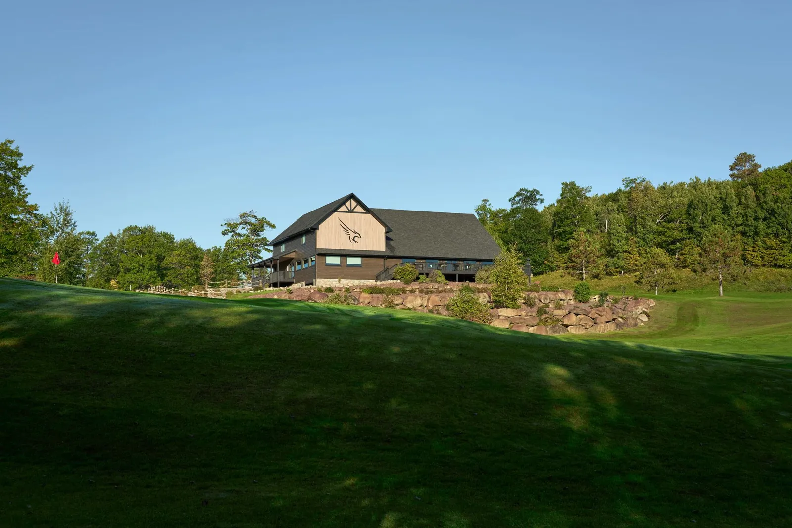 Distant view of the Golden Eagle clubhouse perched on a rock-walled rise, with a red pin flag in the foreground green