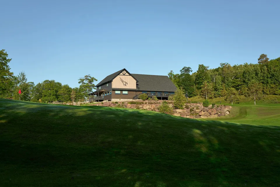 Distant view of the Golden Eagle clubhouse perched on a rock-walled rise, with a red pin flag in the foreground green