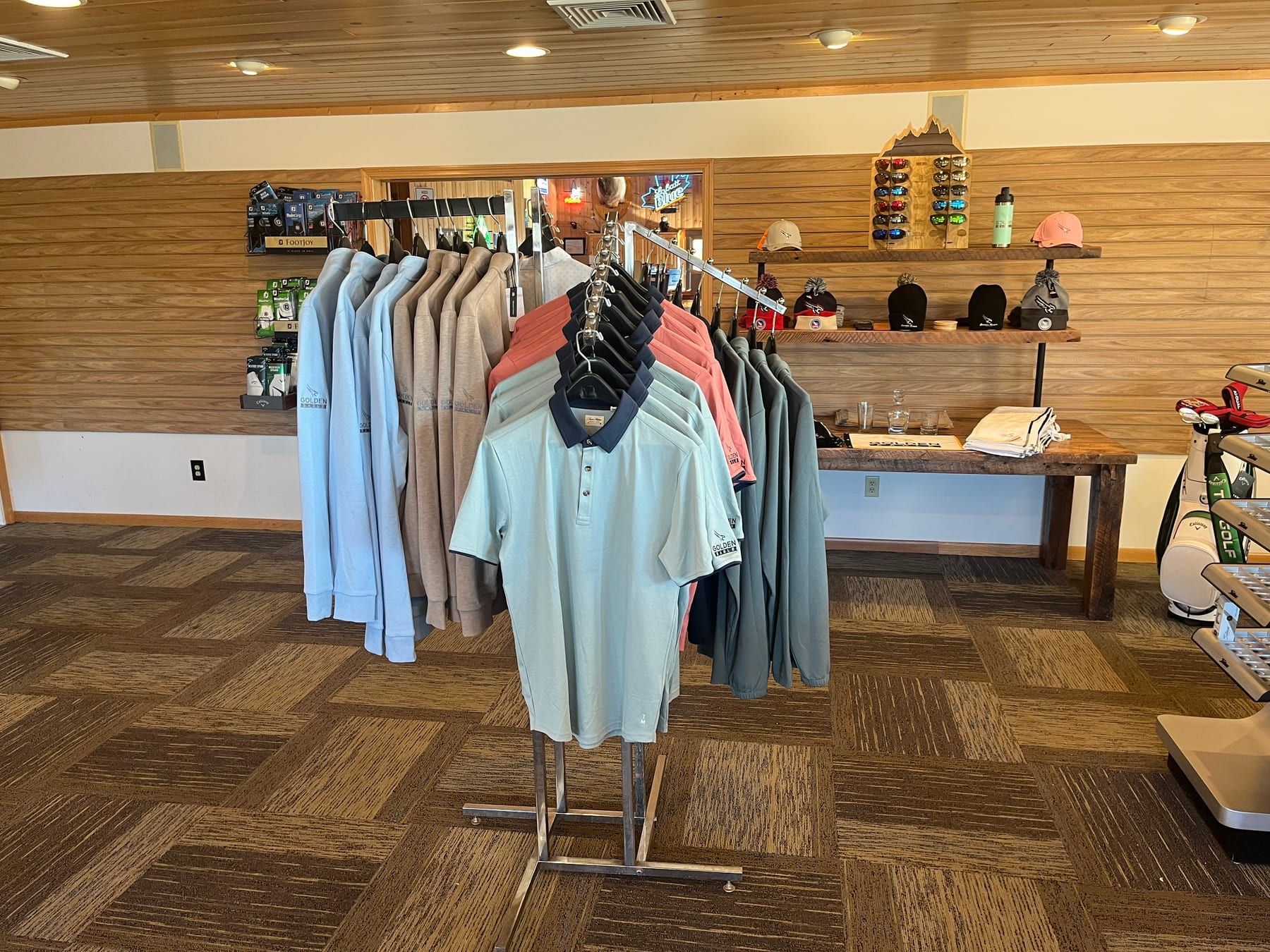 Polo shirts on a round rack inside the Golden Eagle pro shop with the hat wall and accessories displayed in the background