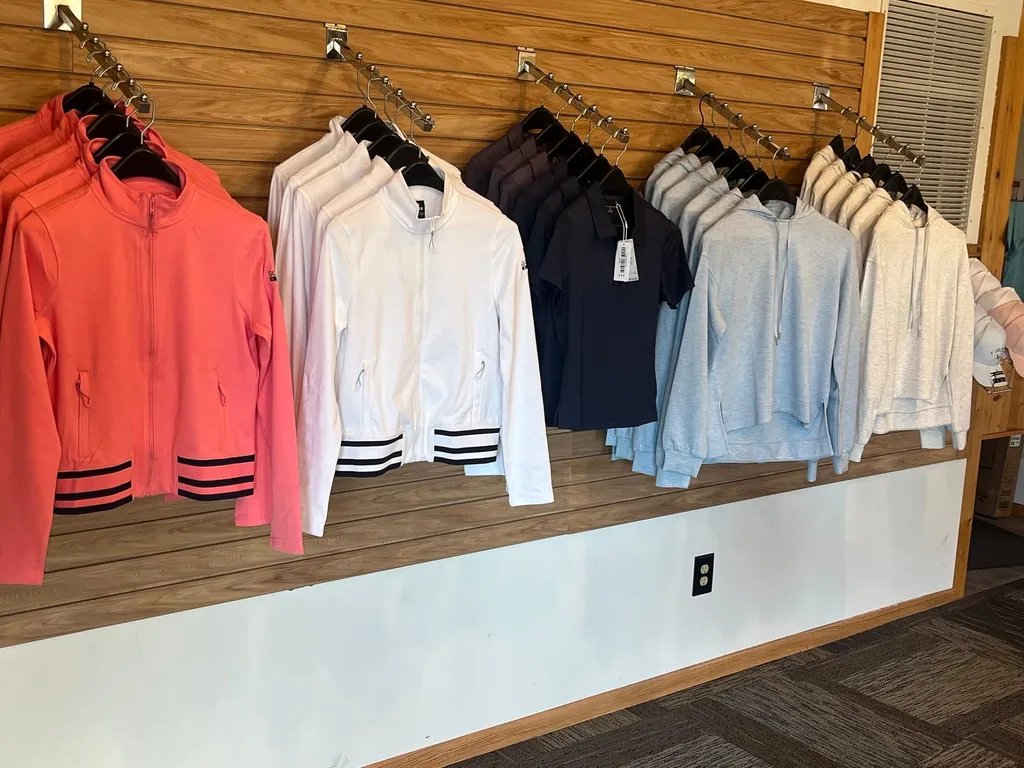 Women's jackets and hoodies in coral, white, navy, and gray hanging along the pro shop wall
